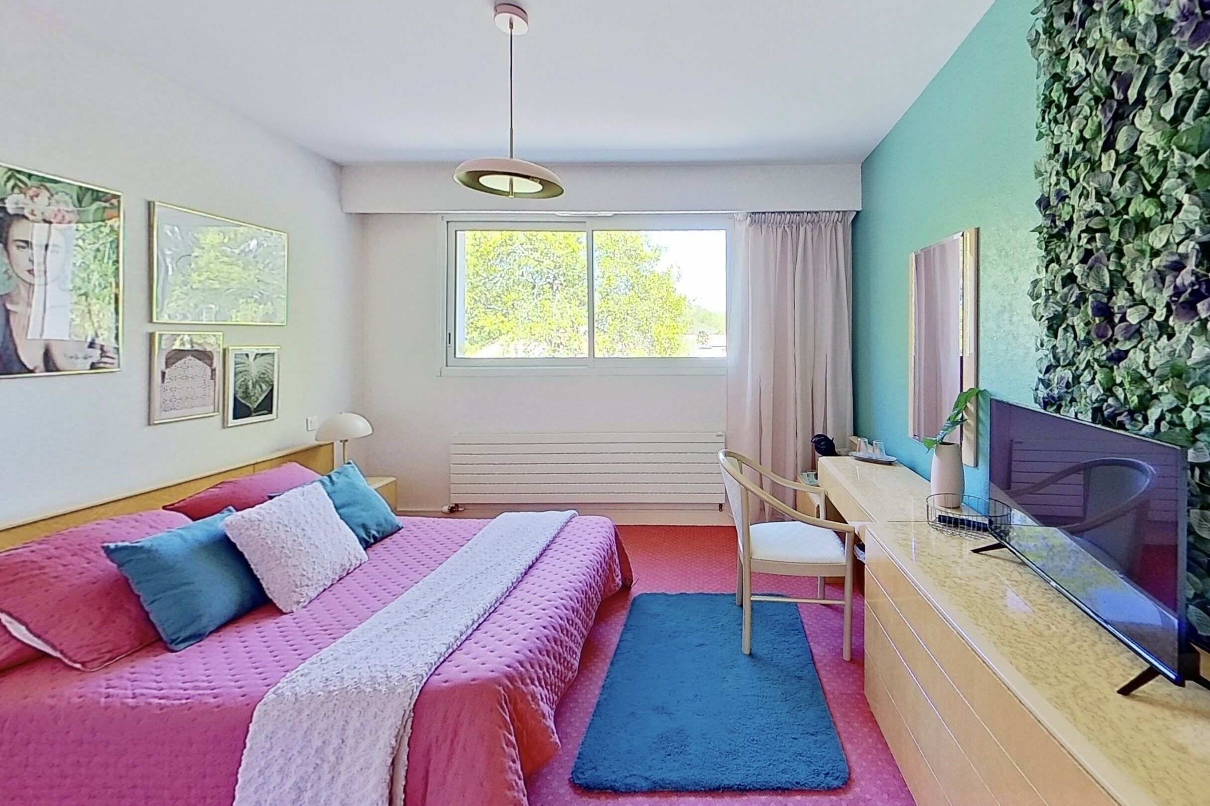 Une chambre à coucher avec un lit, un bureau, une chaise, une télévision et une fenêtre avec des rideaux.