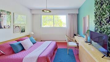 Une chambre à coucher avec un lit, un bureau, une chaise, une télévision et une fenêtre avec des rideaux.