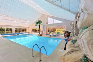 An indoor swimming pool with clear blue water, surrounded by lounge chairs and a rock-like wall feature. - Les Jardins de la Muse / BnB maison d'hôte, piscine couverte et spa (Basse-Goulaine)