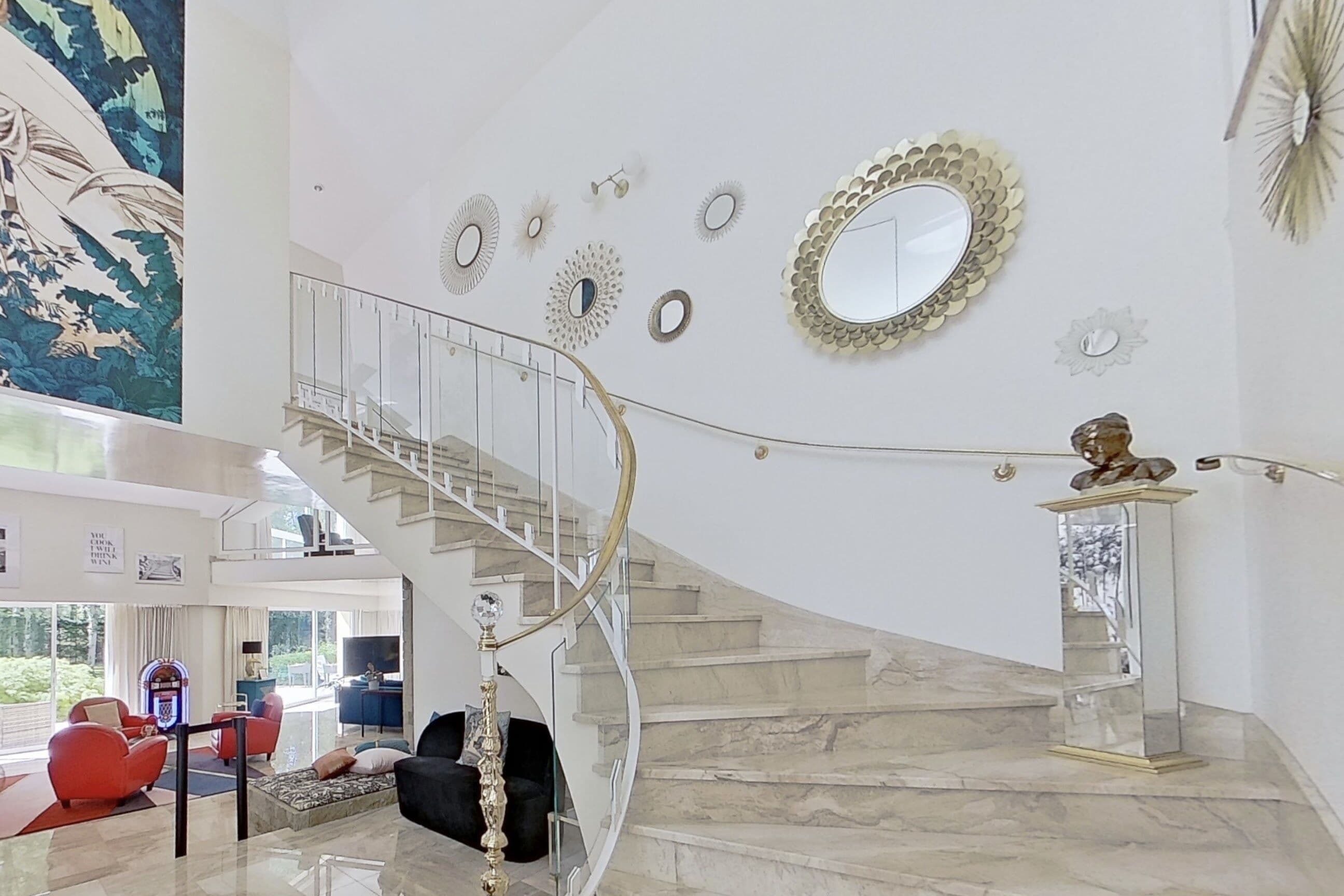 Ein geräumiger Wohnbereich mit einer geschwungenen Treppe, einem großen Spiegel und einer dekorativen Statue.