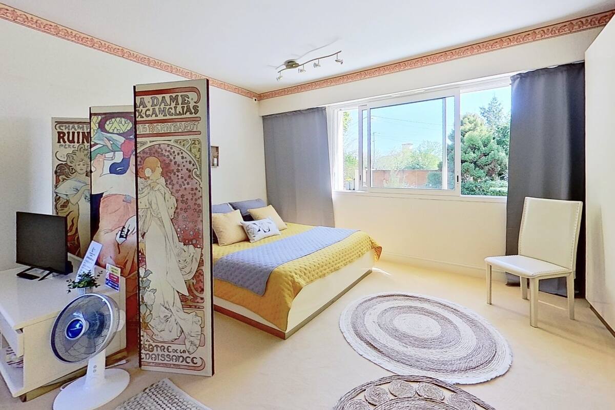 A bedroom with a bed, a desk with a computer, a chair, and a window with curtains.