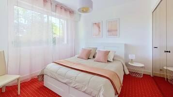 Une chambre à coucher avec un lit, une chaise, une table de chevet avec une lampe et une fenêtre avec des rideaux.
