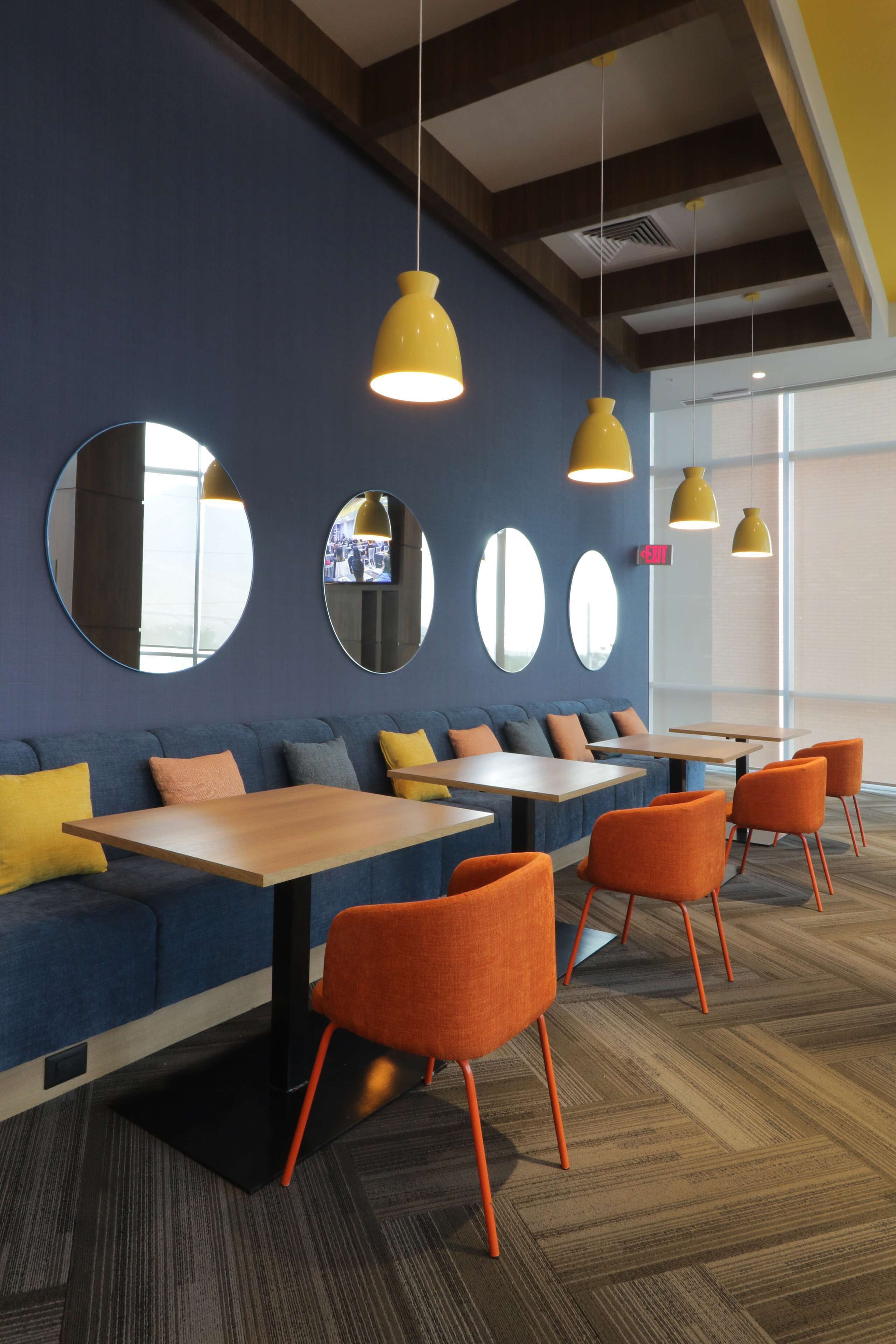 Een modern interieur met een blauwe bank, oranje stoelen en houten tafels.