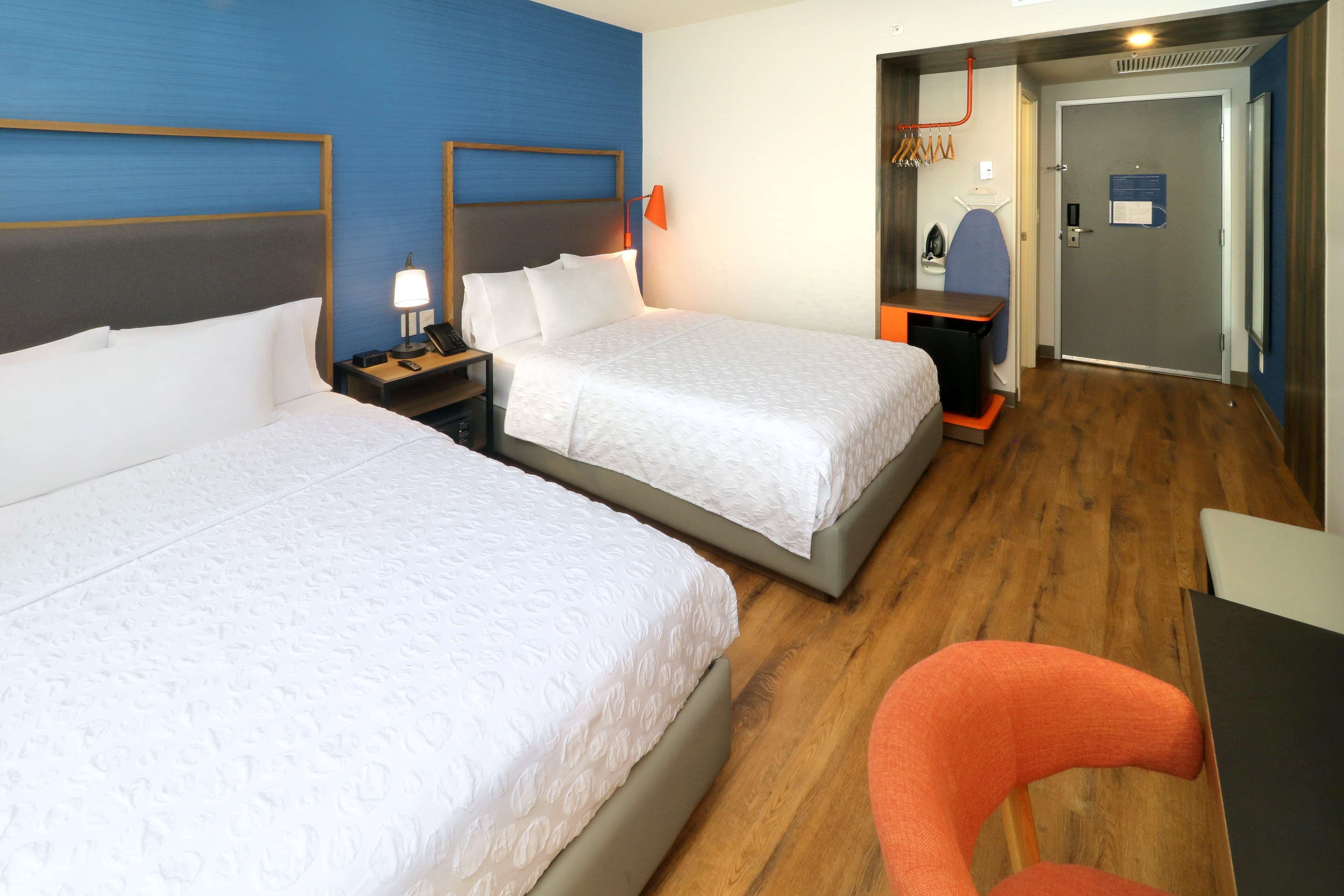 A hotel room with two beds, a desk, a chair, and a door leading to a bathroom.