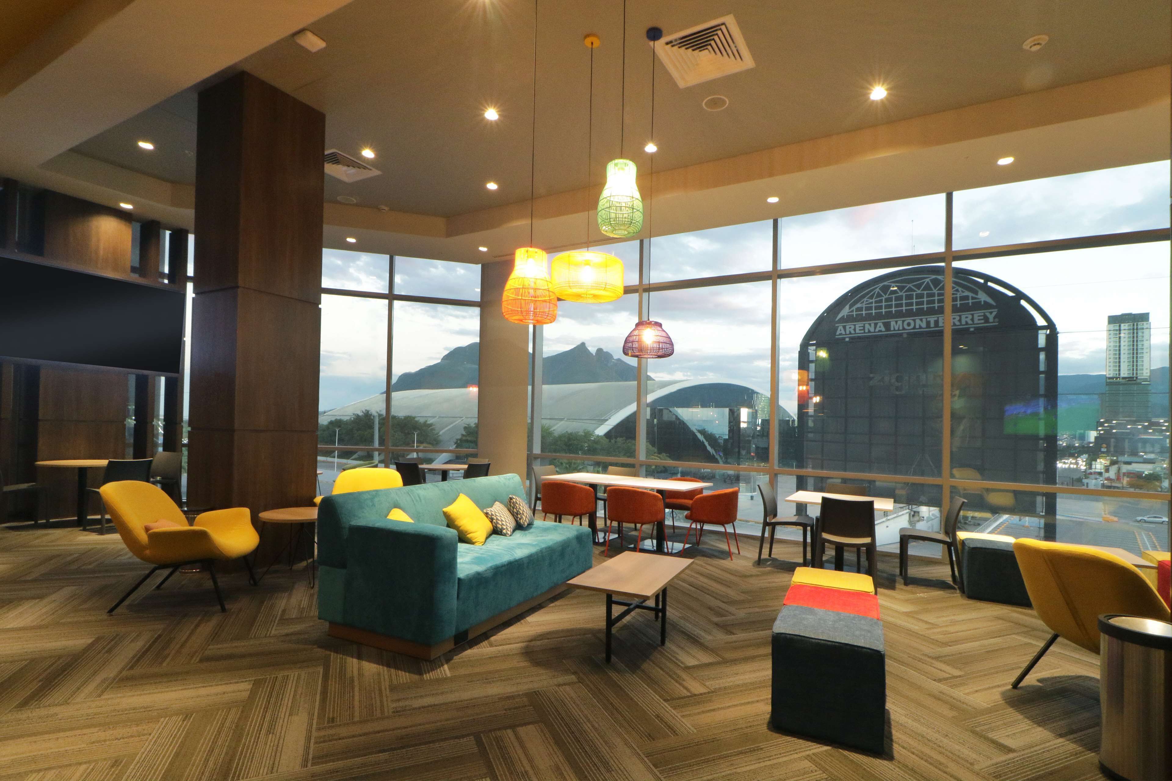 A modern hotel lobby with a large seating area, a view of the cityscape, and a distinctive building in the background.