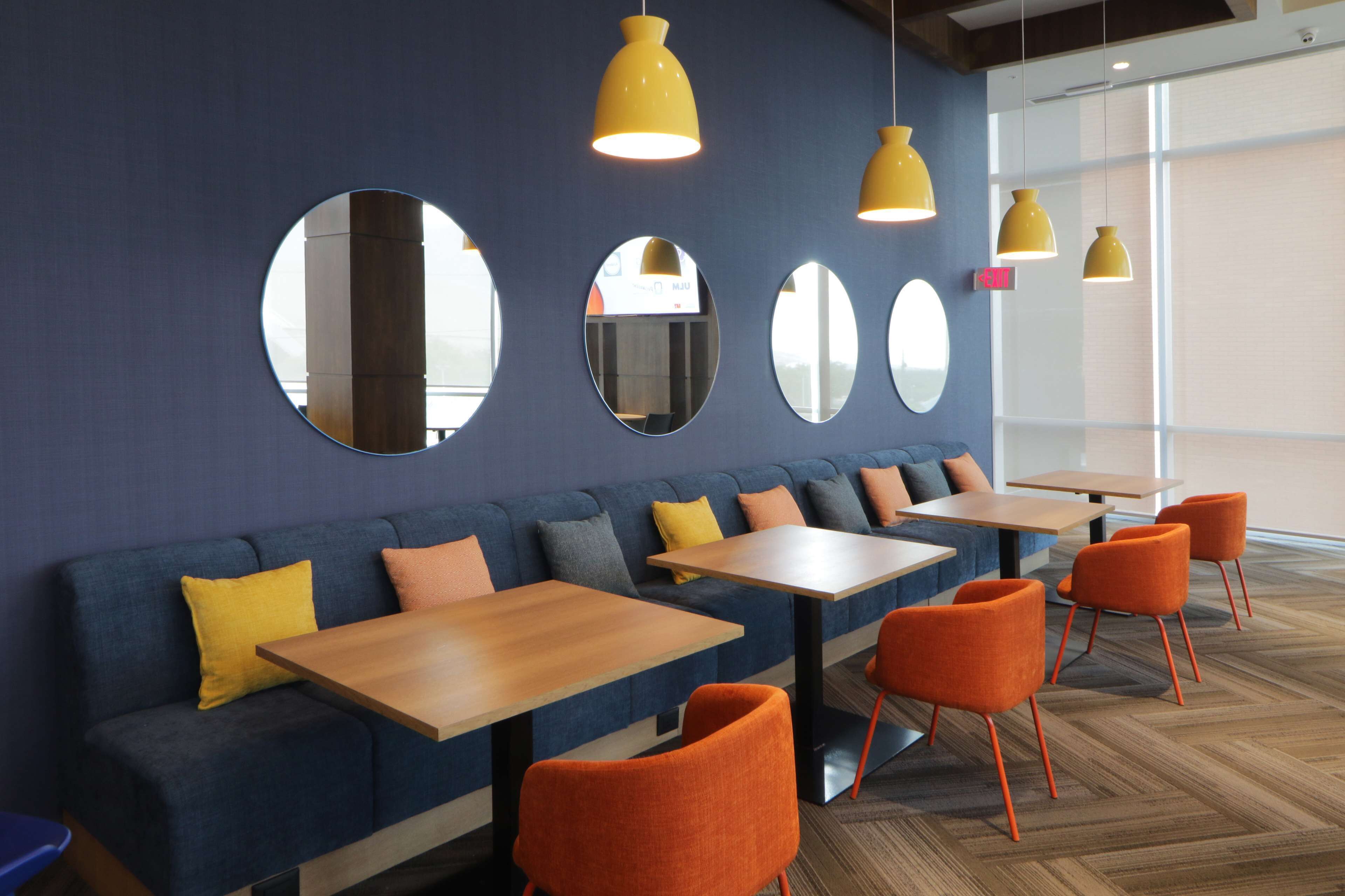 A modern interior with a blue sofa, orange chairs, wooden tables, and yellow pendant lights.