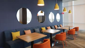 A modern interior with a blue sofa, orange chairs, wooden tables, and yellow pendant lights.