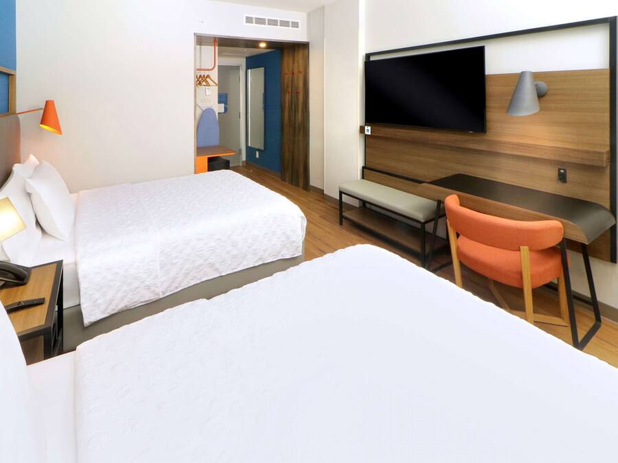Una camera d'albergo con due letti, una scrivania, una sedia, una TV e una lampada.