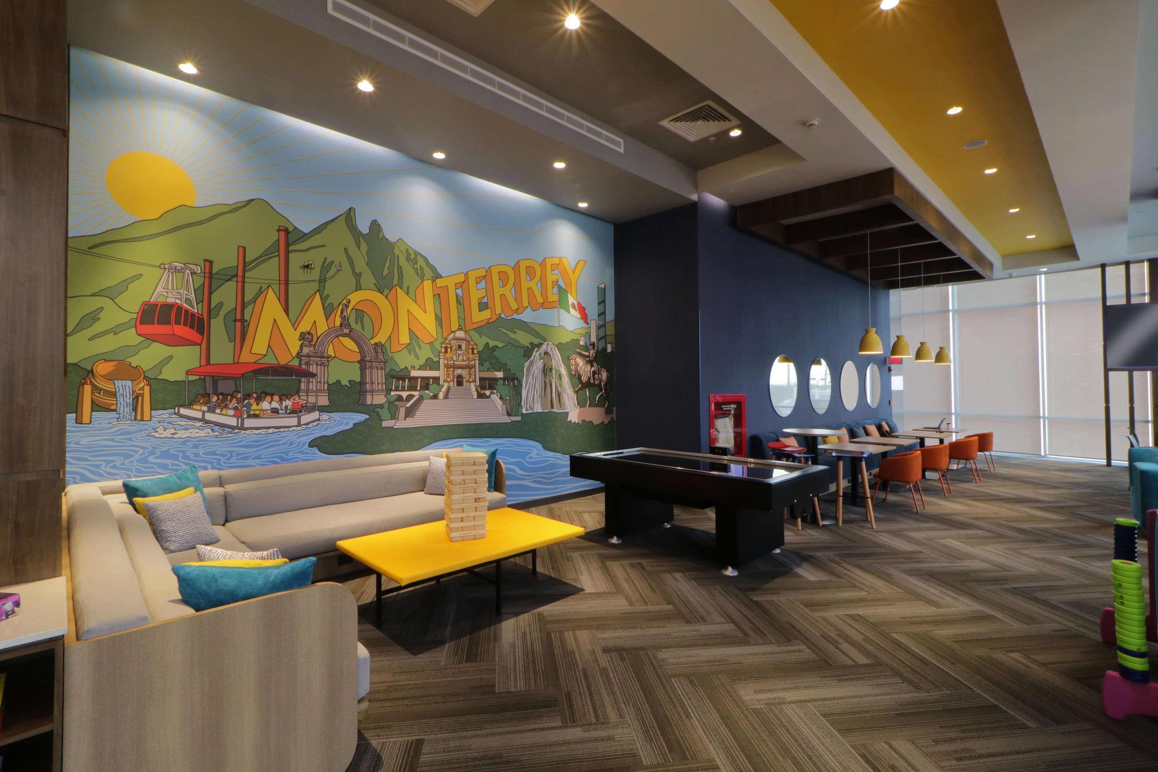 Un espacio de descanso con un mural de Monterrey, una mesa de billar, sofás y una mesa de ping pong.