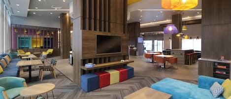 Un moderno vestíbulo de hotel con un televisor grande, zonas de estar y un bar.