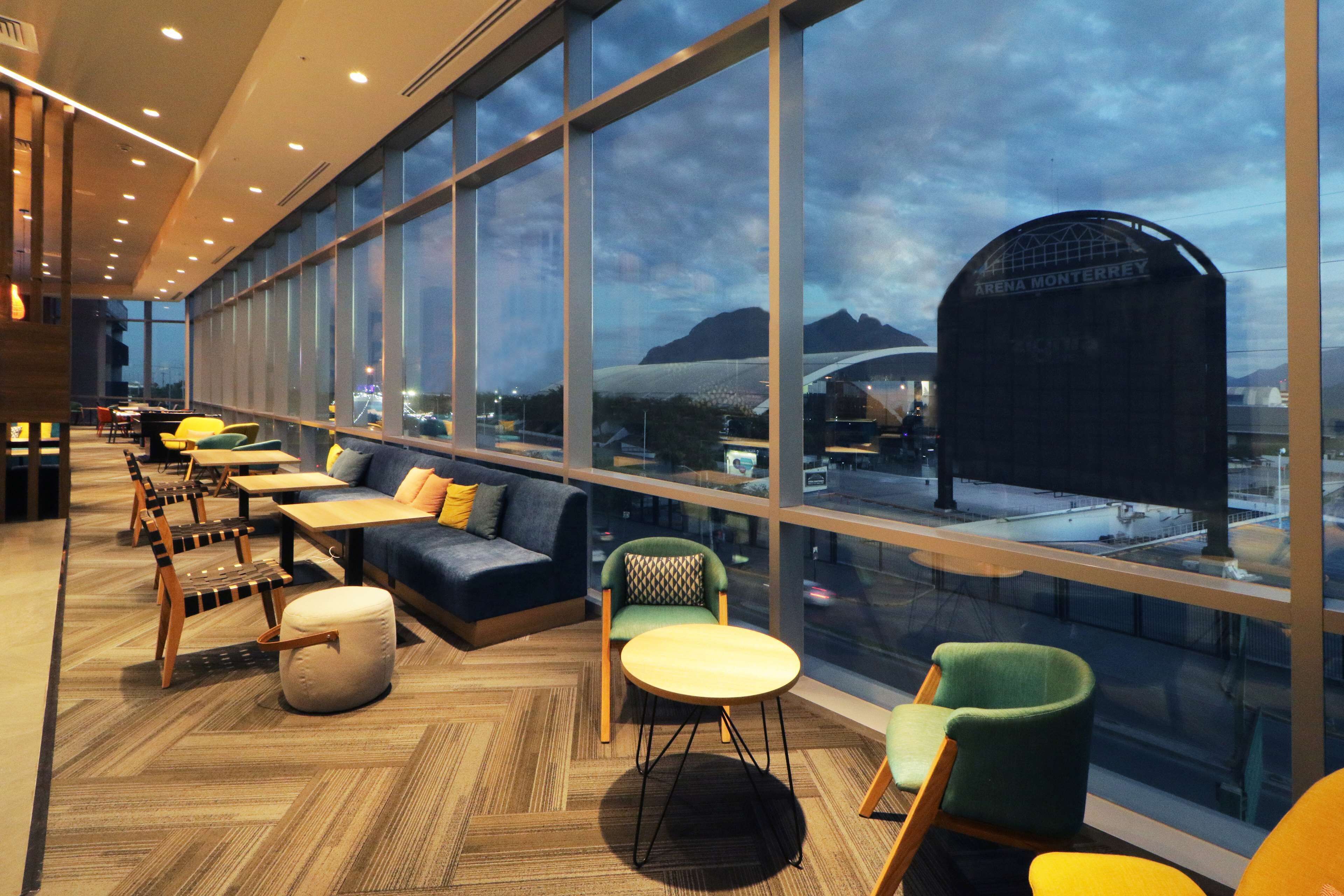 A modern lounge area with seating arrangements, large windows, and a view of a stadium.