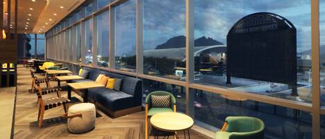 A modern lounge area with seating arrangements, large windows, and a view of a stadium.