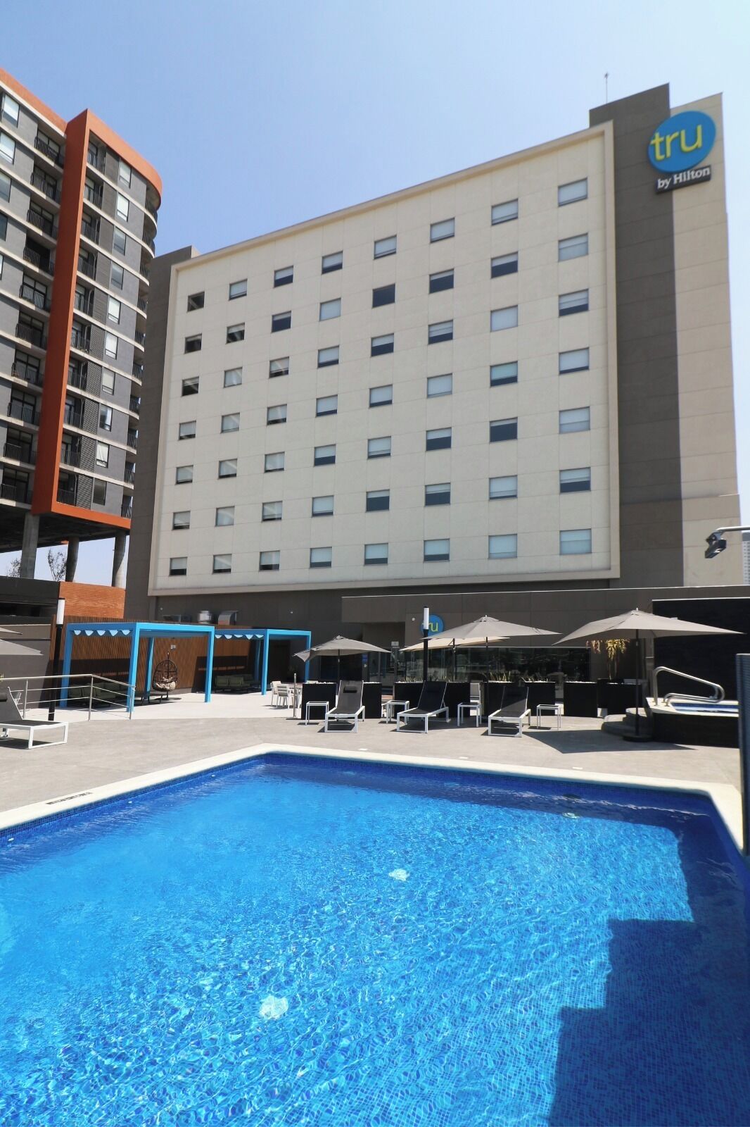 Un hôtel doté d’une piscine, d’un espace extérieur aménagé et d’un grand bâtiment comportant plusieurs étages et des balcons.