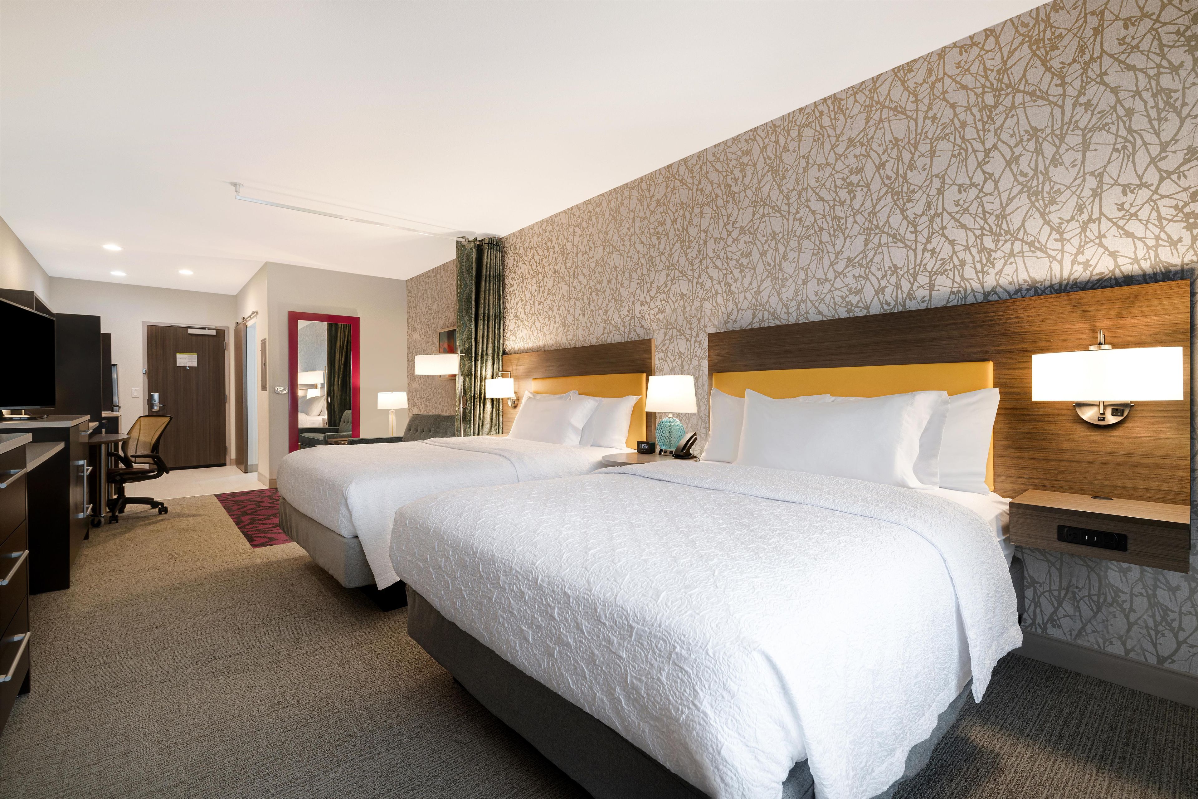 A hotel room with two beds, a desk, a chair, and a television.