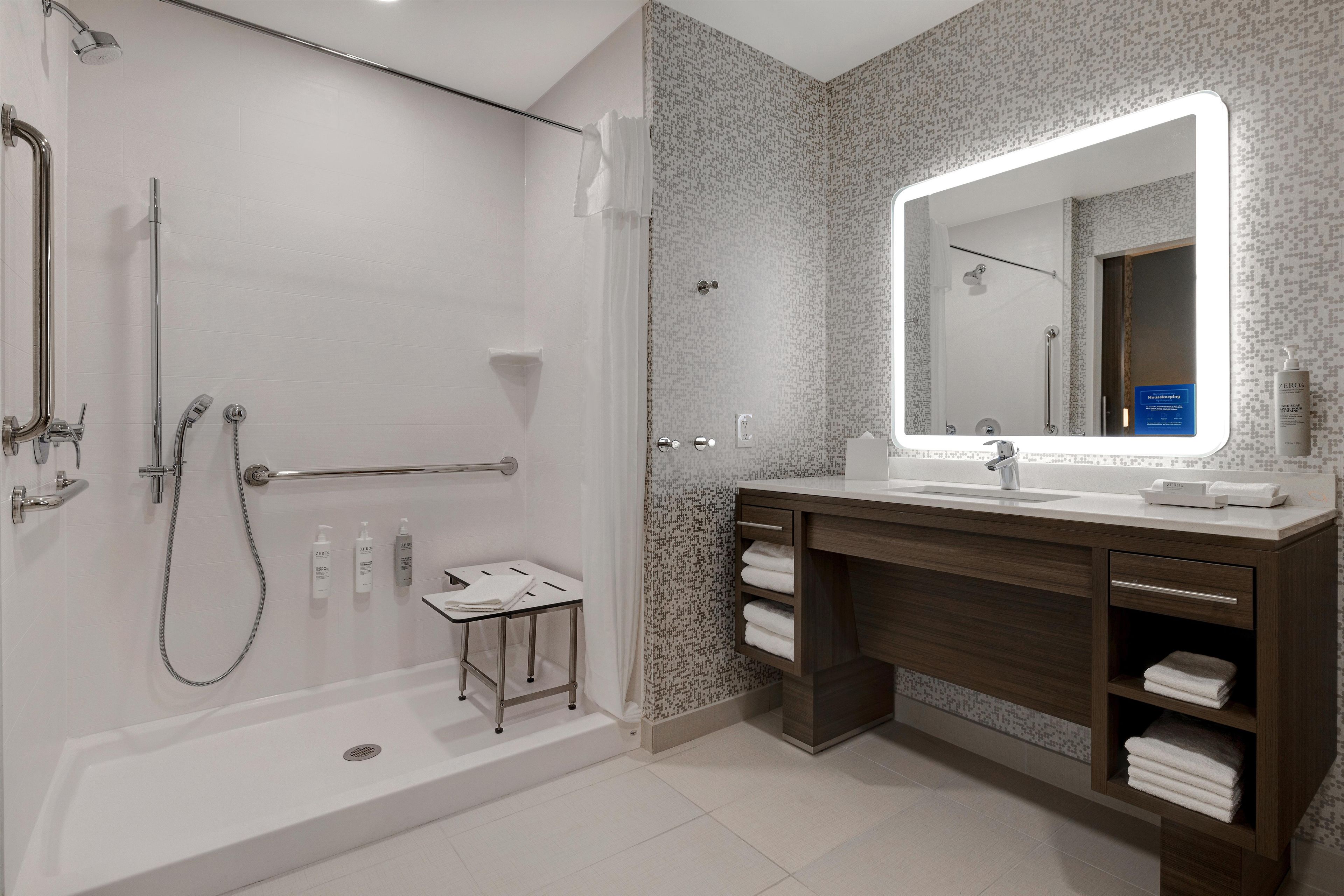 A modern bathroom with a walk-in shower, a large mirror, and a vanity with a towel rack.