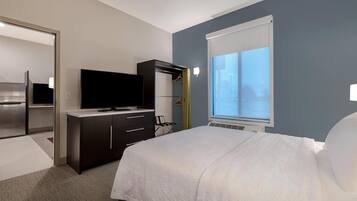 A hotel room with a bed, a flat-screen TV, a dresser, and a window with blinds.