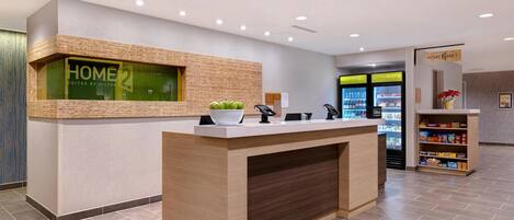 A hotel reception area with a wooden reception desk, a digital display, and vending machines.