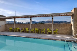 A poolside area with a covered seating area, chairs, and a view of mountains. - Home2 Suites By Hilton Redding (Redding)