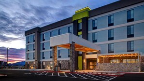 A multi-story hotel with a covered entrance, stone pillars, and a parking lot. - Home2 Suites By Hilton Redding (Redding)