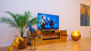 Un salon moderne doté d’un téléviseur à écran plat, d’une statue de paon décorative, d’une grande plante, d’une cheminée et d’un lampadaire sphérique doré.