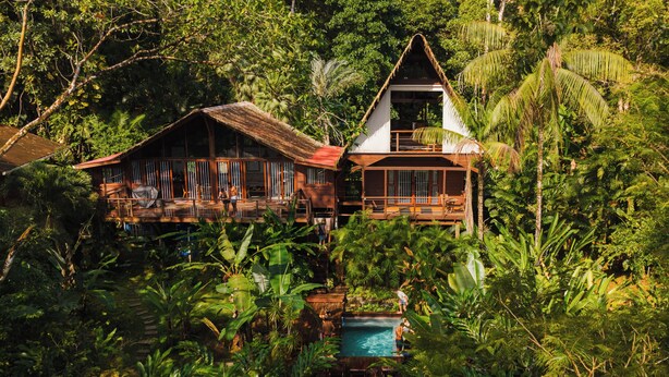 Ein tropisches Resort mit Holzbauten, einem Pool und üppiger Vegetation.