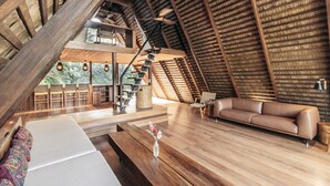 Ein Innenraum mit schrägen Deckenbalken, einer Couch, einem Esstisch und einer Treppe.