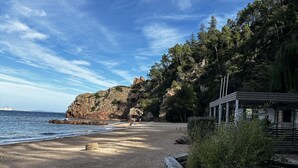 A beach with a rocky cliff, a wooden fence, and a building with a sloped roof.