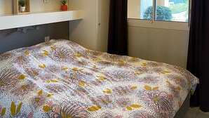 A bedroom with a bed, a ceiling light, a window with curtains, and a shelf with decorative items.