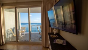 A room with a balcony, a TV, and a desk with a chair.