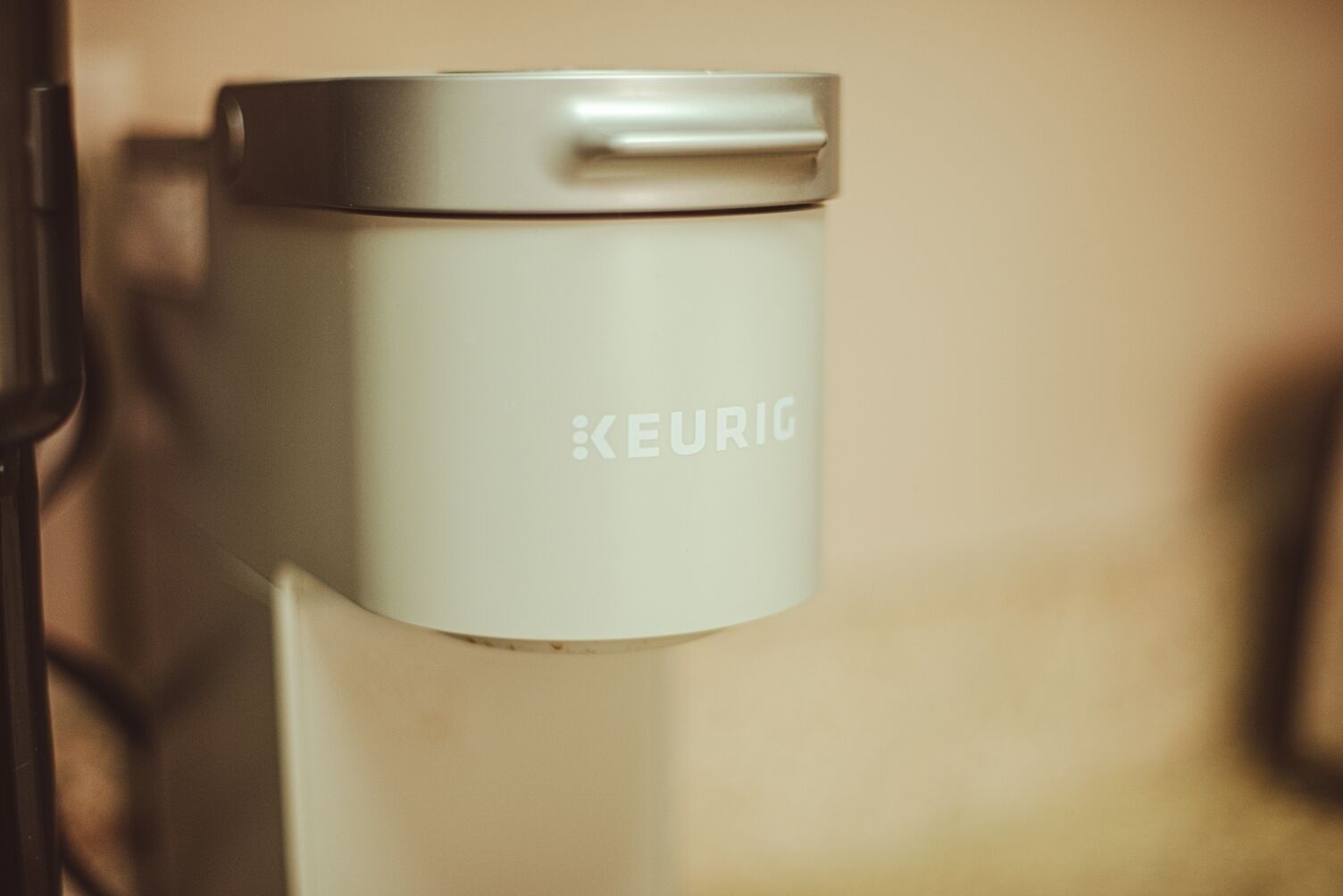 Een witte KEURIG koffiezetapparaat met een deksel op een wandmontage.