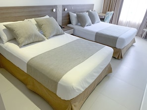 A hotel room with two beds, each with a wooden headboard and white bedding. There are two bedside tables with lamps, and a window with curtains. - Hotel 1525 By Geh Suites (Santa Marta)