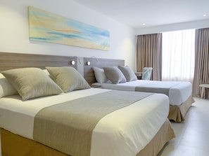 A hotel room with two beds, a headboard, bedside lamps, a large abstract painting, and a window with curtains. - Hotel 1525 By Geh Suites (Santa Marta)