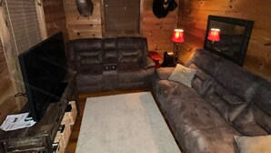 Interior acogedor de una cabaña con sofá seccional, televisor y chimenea.
