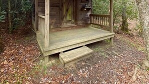 Una cabaña de madera rústica con porche, rodeada de un bosque denso.