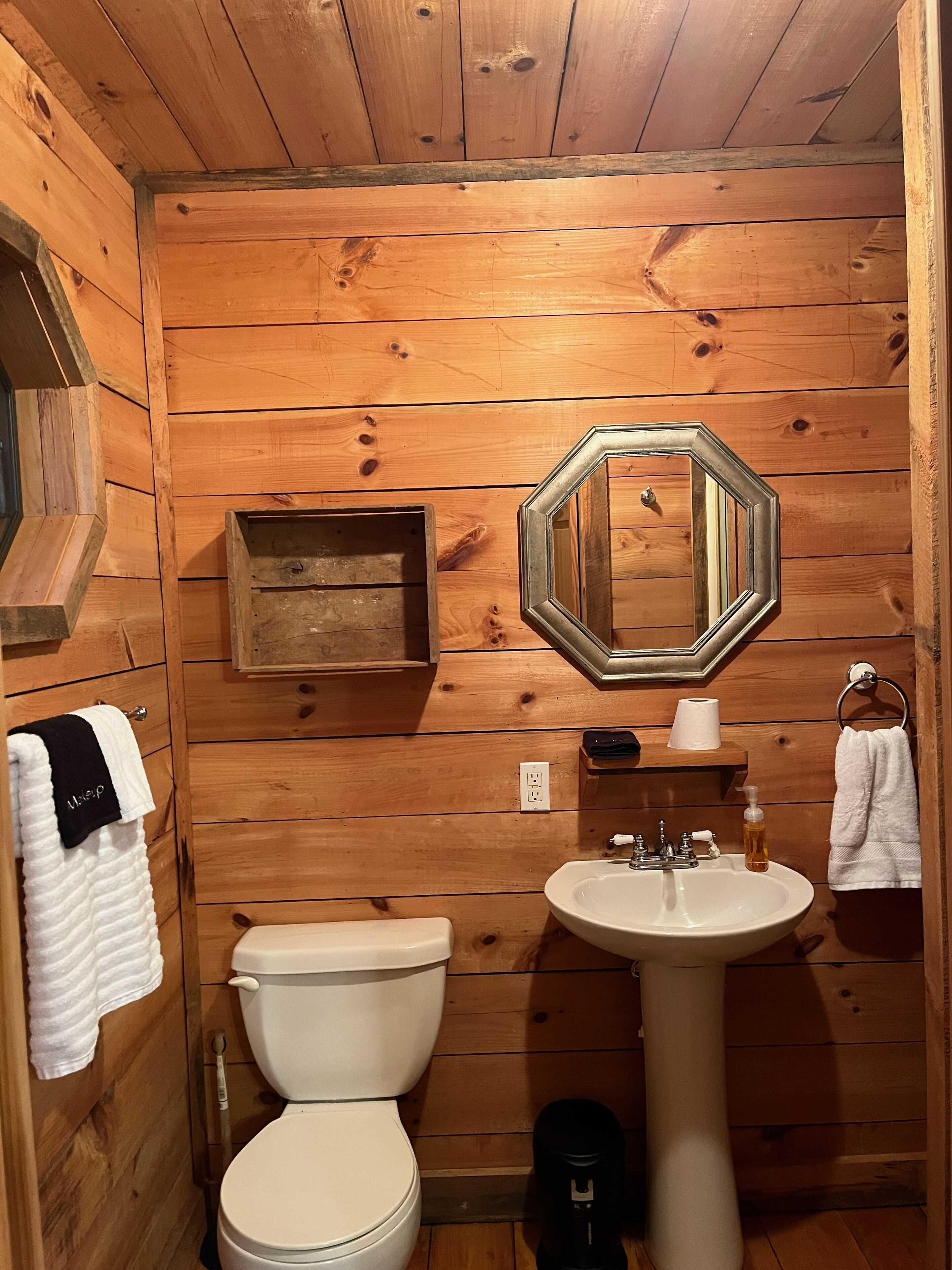 Een badkamer met houten lambrisering, voorzien van toilet, wastafel, spiegel, handdoekhouder en een klein houten plankje.