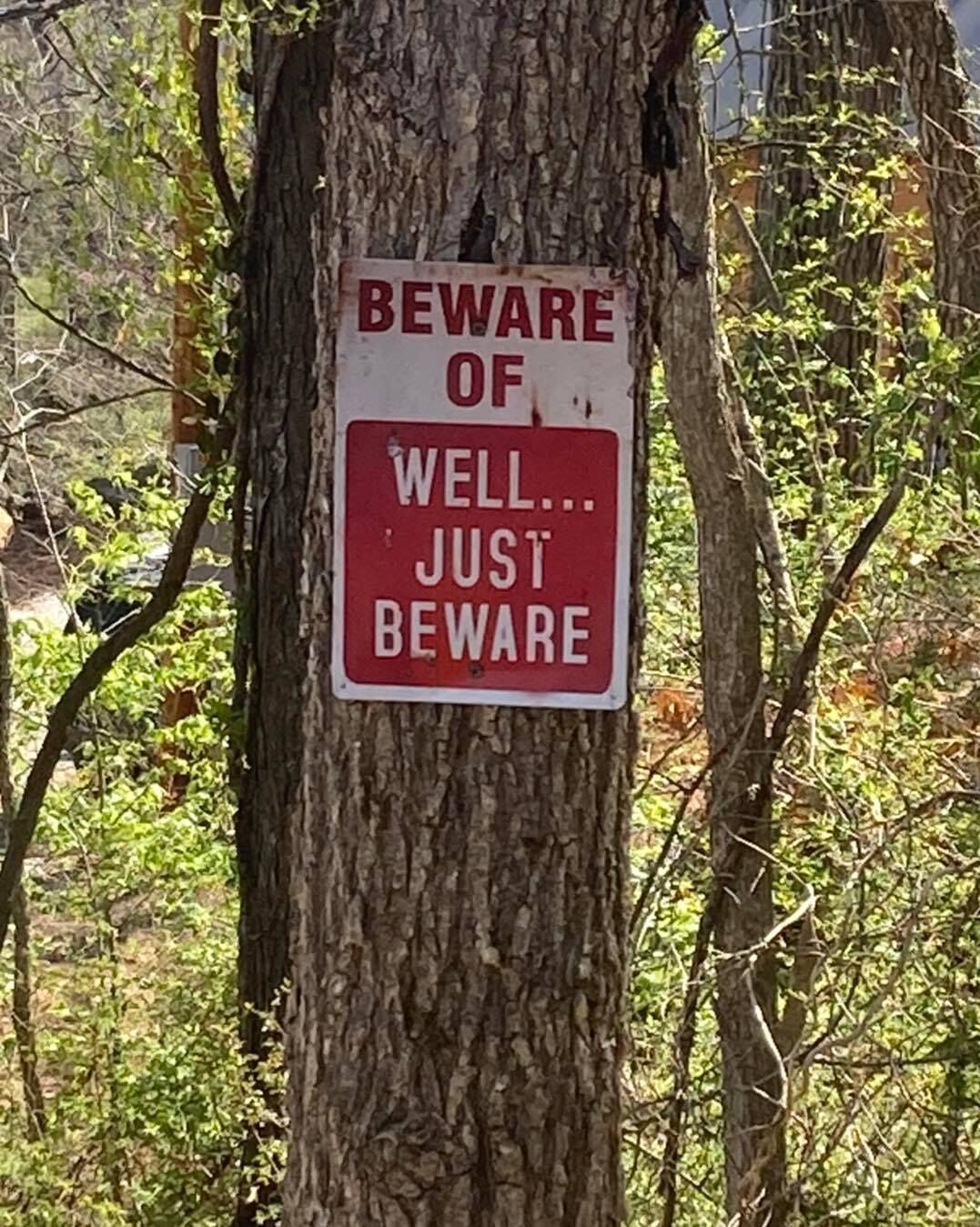 A sign on a tree trunk with the text "BEWARE OF WELL... JUST BEWARE".