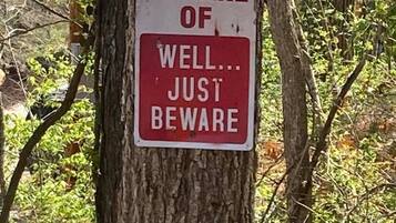 A sign on a tree trunk with the text "BEWARE OF WELL... JUST BEWARE".
