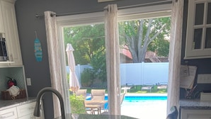 Eine Küche mit einer Granit Arbeitsplatte, schwarzen Ledersitzhocker und Blick auf einen Garten mit Pool und Gartenmöbeln.