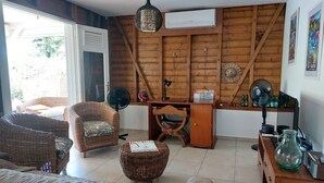 A cozy room with wicker furniture, a desk with a computer, a fan, and a large window.