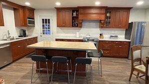 Una cocina moderna con armarios de madera, una isla central con taburetes de bar, electrodomésticos de acero inoxidable y un ventanal con vistas.