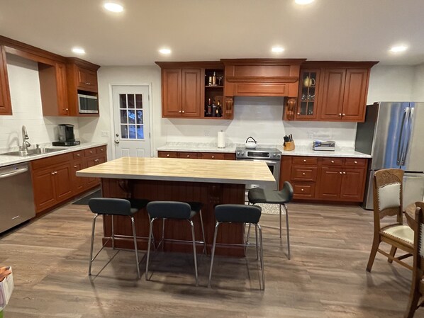 A modern kitchen with wooden cabinets, a central island with bar stools, stainless steel appliances, and a window with a view.