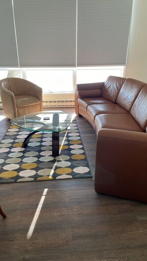 A living room with a brown leather sofa, a glass coffee table, a patterned rug, and a beige armchair.