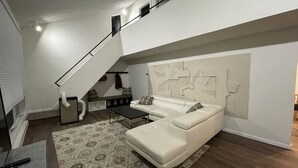 Una sala de estar moderna con un sofá blanco, una alfombra estampada y una escalera que lleva a un nivel superior.