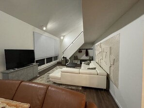 A modern living room with a flat-screen TV, a white sofa, a brown leather couch, and a staircase leading to an upper level.