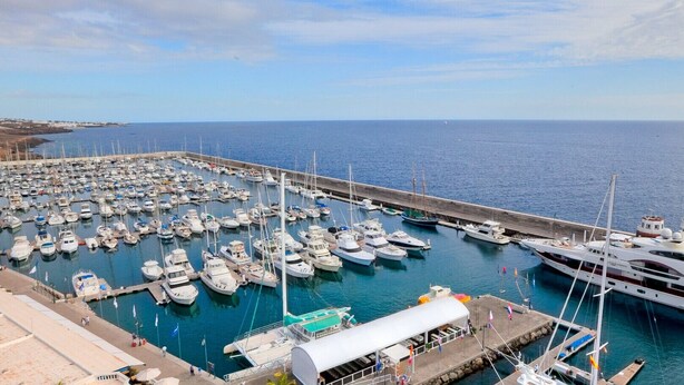 A marina with numerous boats docked, a large yacht, and a pier extending into the water. - Casa Kaliste (Puerto Calero)