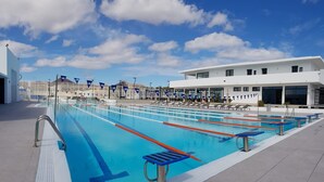A large outdoor swimming pool with multiple lanes, surrounded by lounge chairs and a modern building in the background. - Casa Kaliste (Puerto Calero)