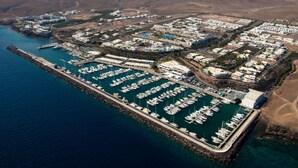 An aerial view of a marina with numerous boats docked, surrounded by residential buildings and a mountainous backdrop. - Casa Kaliste (Puerto Calero)