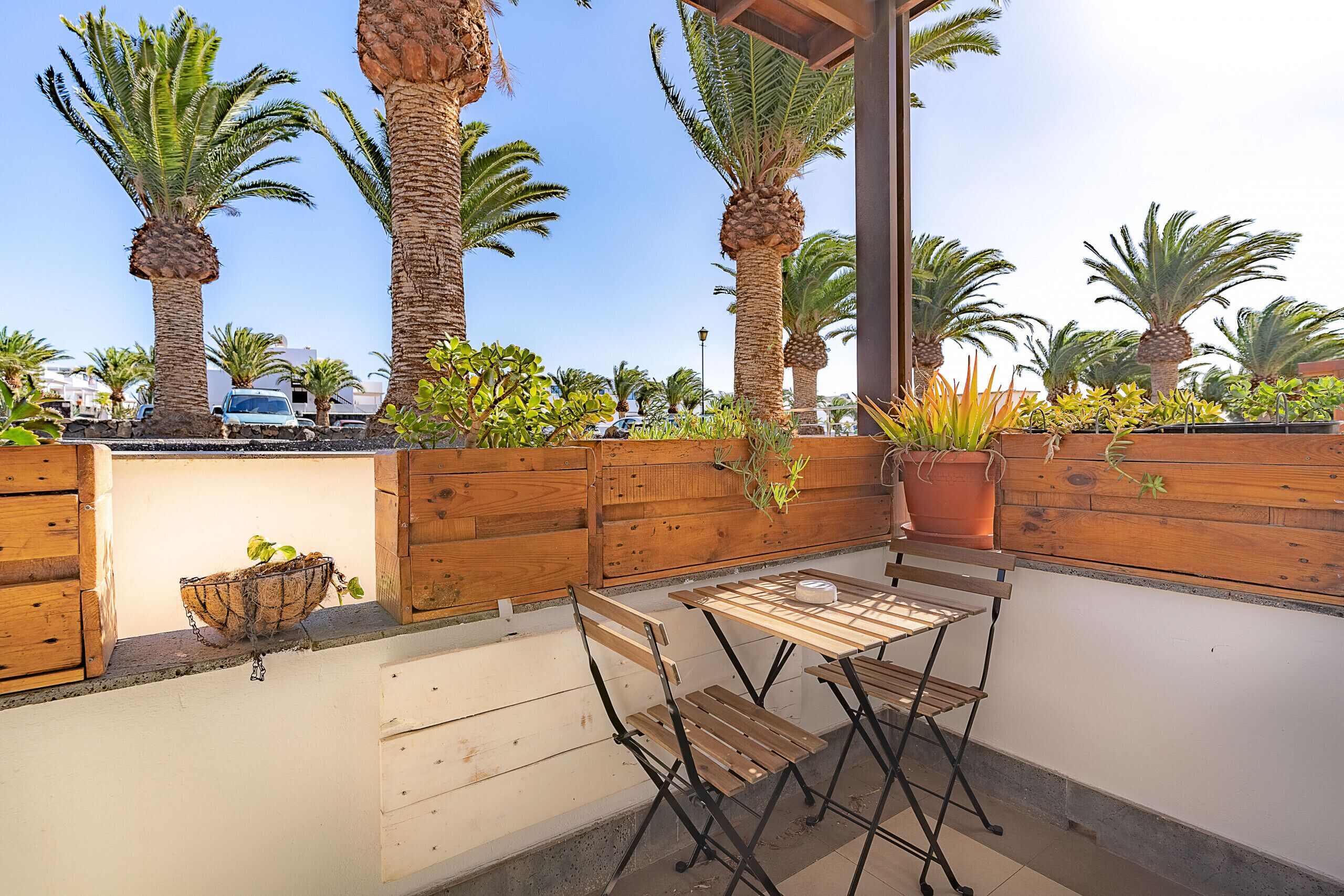 An outdoor patio with wooden furniture, a wooden wall, and several potted plants.