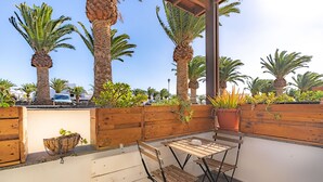 An outdoor patio with wooden furniture, a wooden wall, and several potted plants. - Casa Kaliste (Puerto Calero)