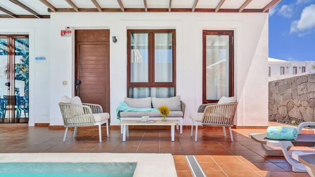 A pool area with a sofa and chairs, a small table with a vase, and a stone wall. - 7 PIEDRAS (Playa Blanca)